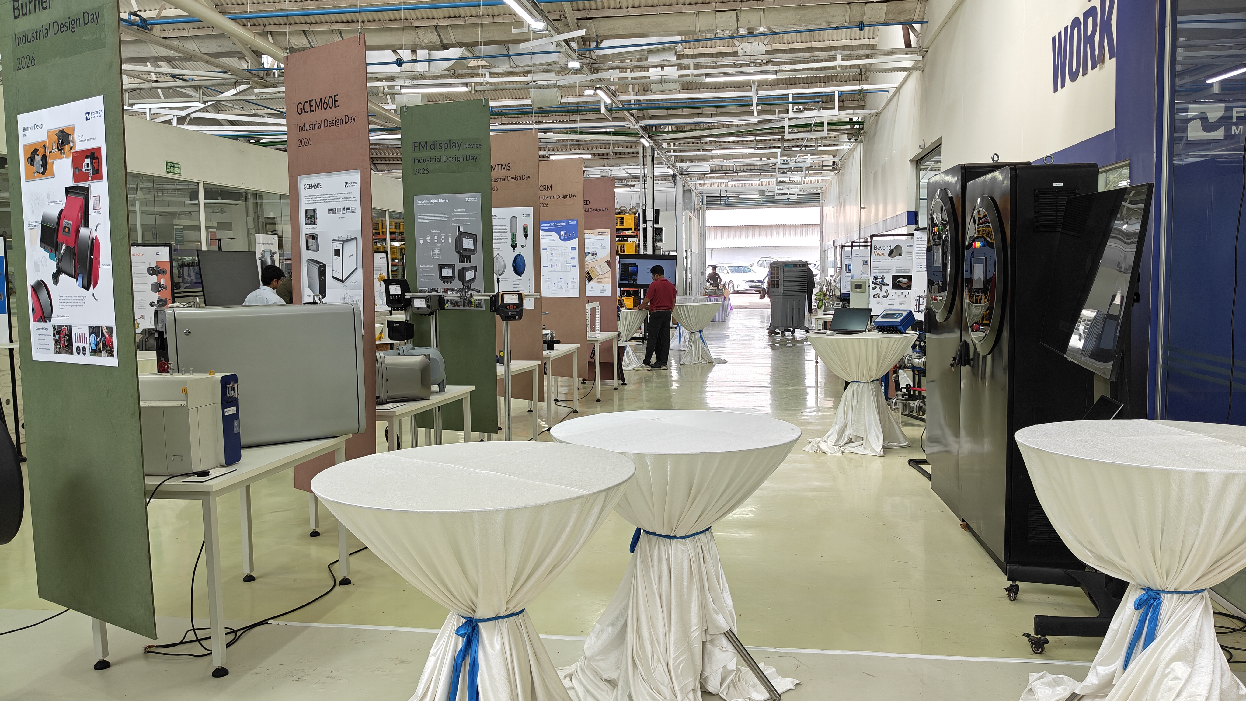 A corridor in the Forbes Marshall R&D building, set up for Industrial Design Day with product display boards along the pillars and tall white-draped tables.