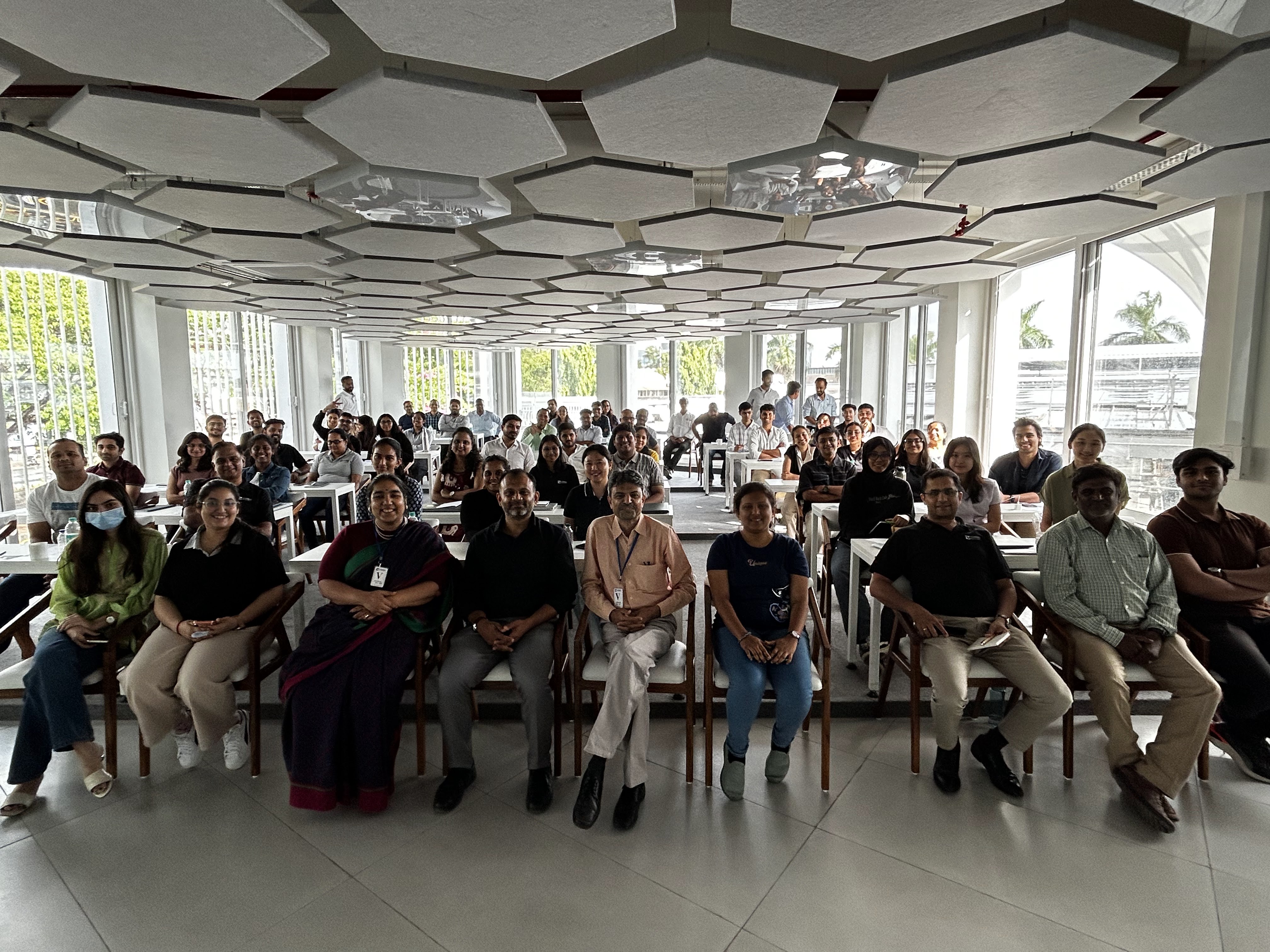 The full training room at Forbes Marshall, rows of people seated under a hexagonal acoustic ceiling, smiling at the camera.