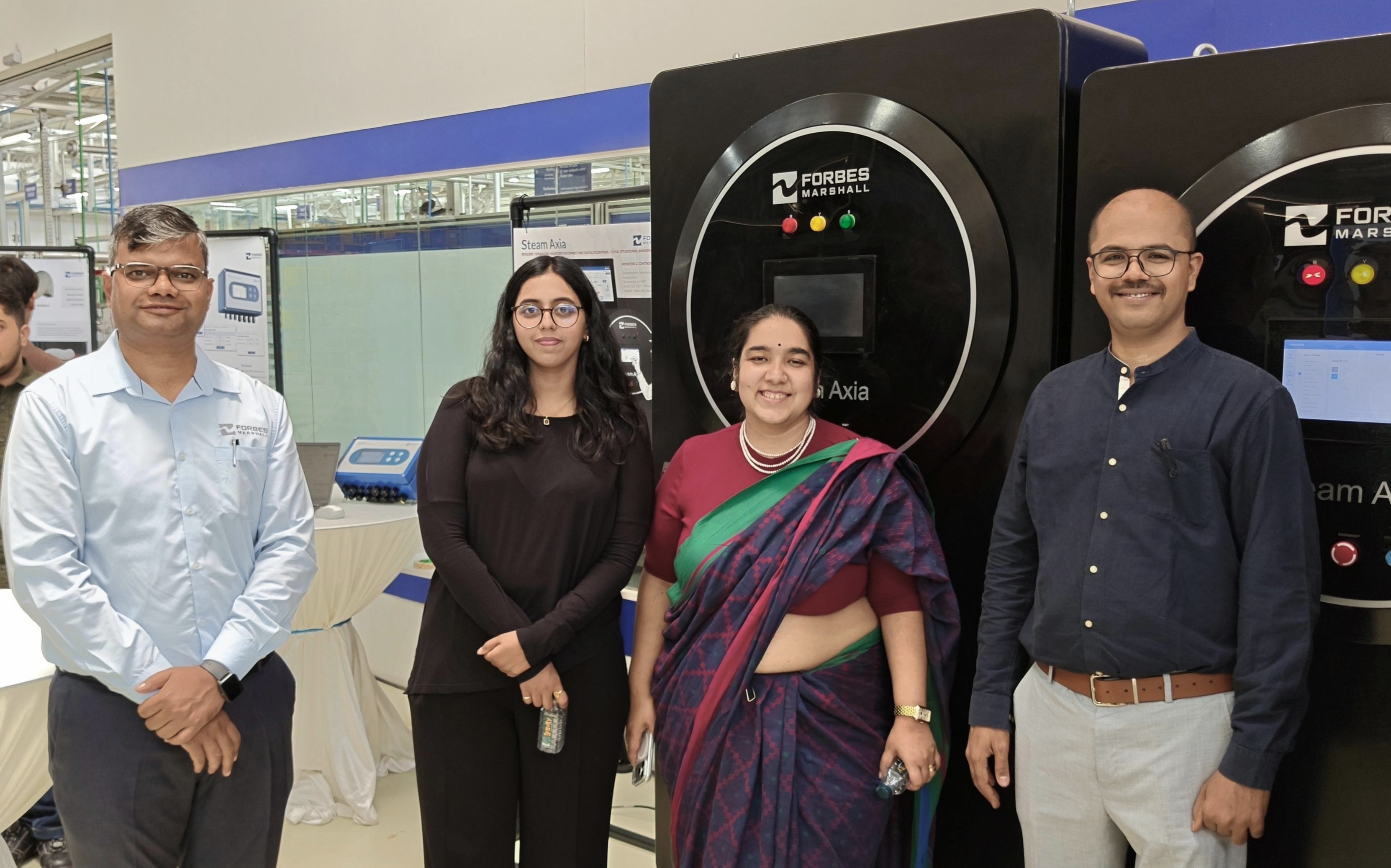 Gurman with three members of the Forbes Marshall team, standing in front of their Steam Axia machines on the factory floor.
